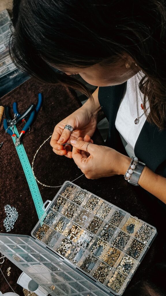 Mujer creando bisutería con alicates, cuentas y materiales en una mesa de trabajo